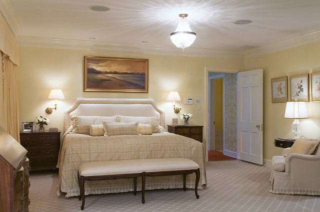 Спальня оформлена в классическом стиле в спокойных пастельных тонах, с хорошо подобранными аксессуарами и светильниками.