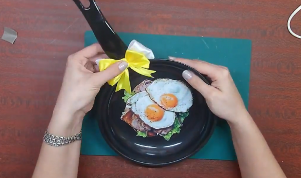 Покройте сковороду прозрачным лаком и приклейте на ручку атласный бант. Украшение для кухни готово