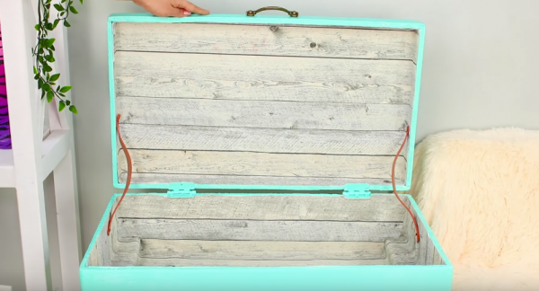 Изнутри чемодан оклеивают обоями с рисунком под дерево. По бокам крепят декоративные ремешки